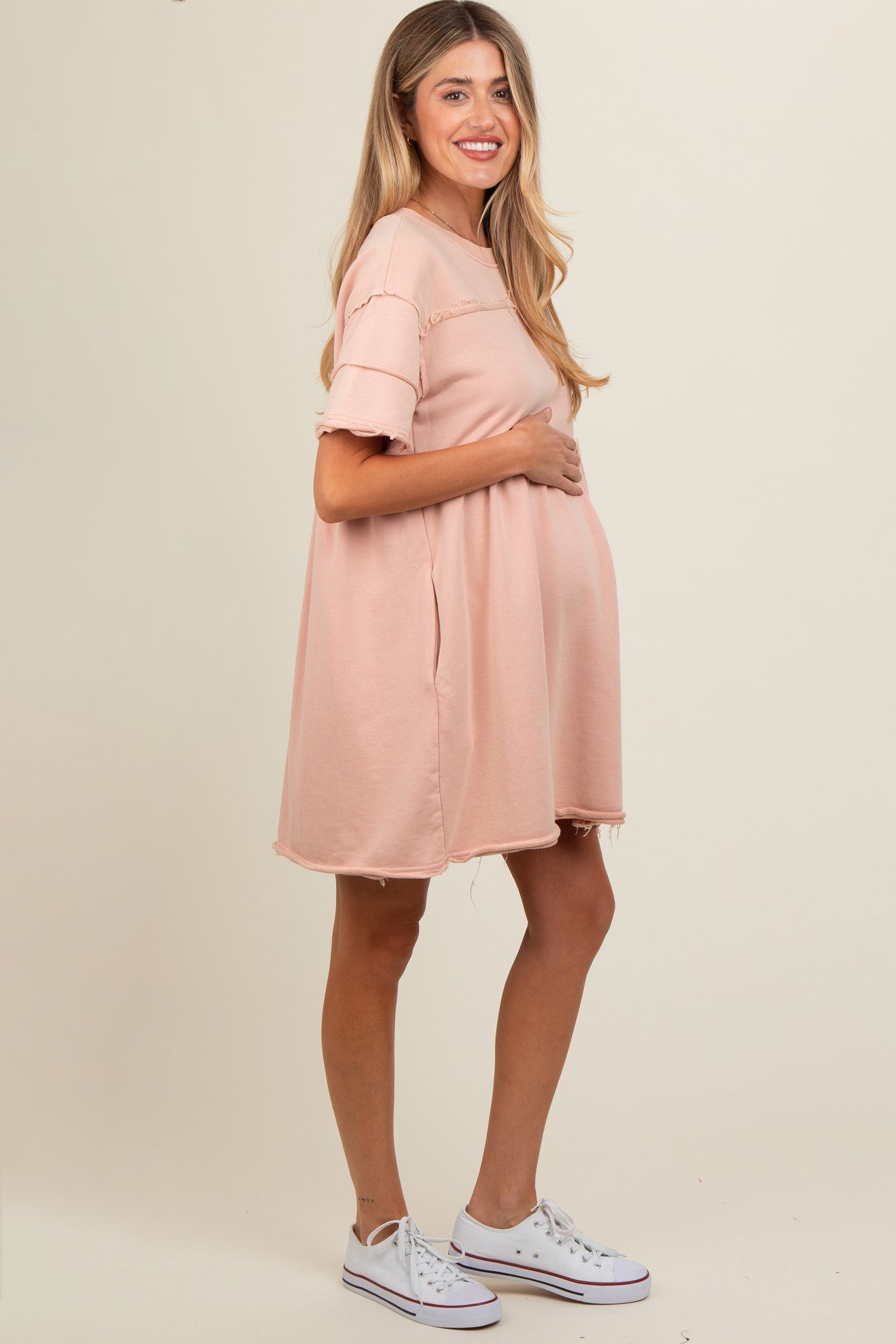 woman wearing a pink maternity dress with short sleeves and frayed hem, holding her baby bump