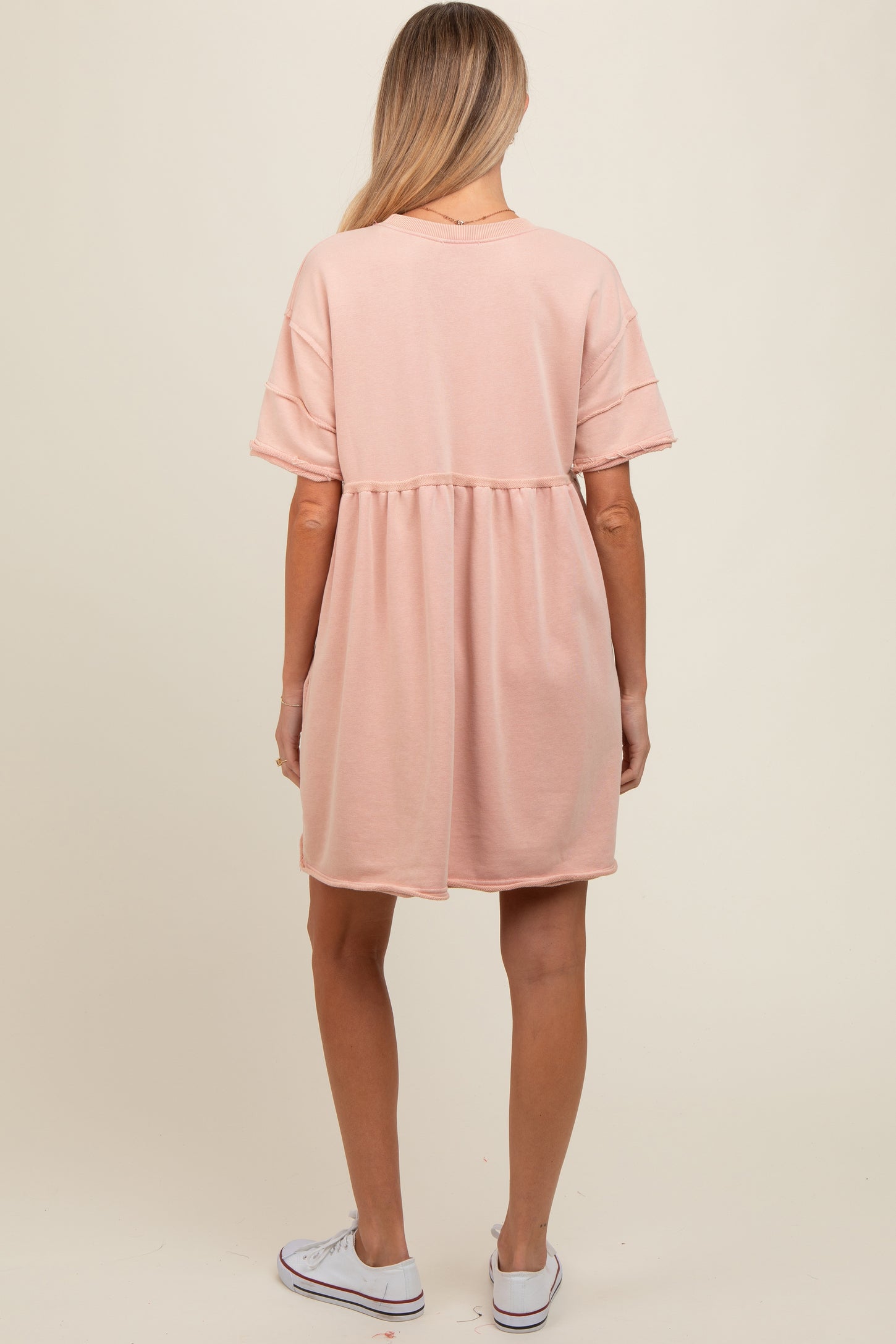 woman wearing a soft pink maternity dress with a relaxed fit and short sleeves, showing her baby bump from the back