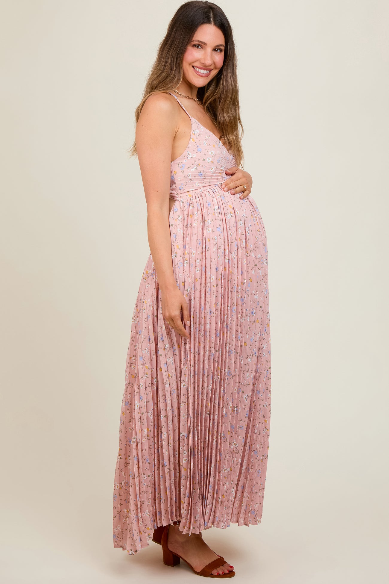 woman wearing a pink floral pleated maternity maxi dress and holding her baby bump