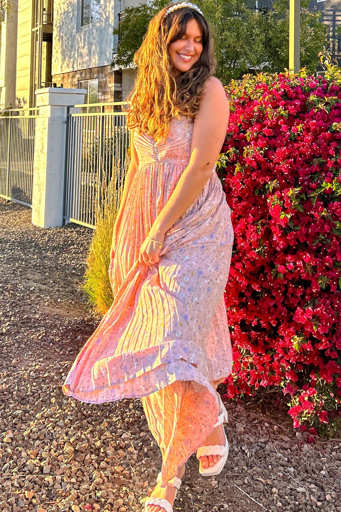 woman wearing a pink floral maxi dress with ruffled edges, twirling in front of blooming flowers