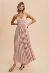 woman wearing a floral maxi dress with pleated details and thin straps, standing against a neutral background