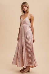 woman wearing a pink floral maxi dress with pleated details and thin straps, standing on a beige background