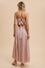 woman wearing a light pink pleated maxi dress with a tie-back detail and floral print, showing the back view