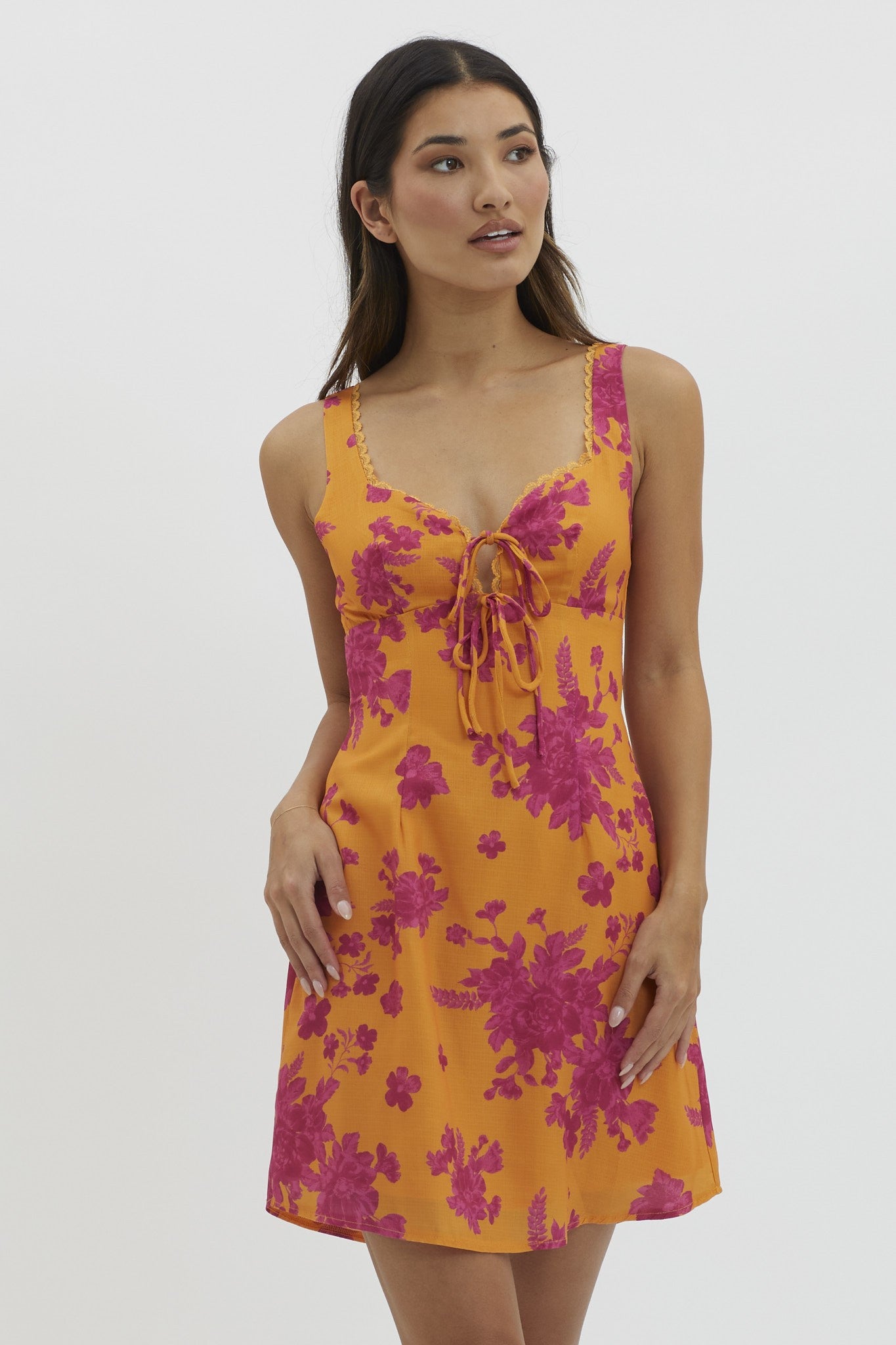 woman wearing a bright orange floral print mini dress with a tie detail at the chest and spaghetti straps