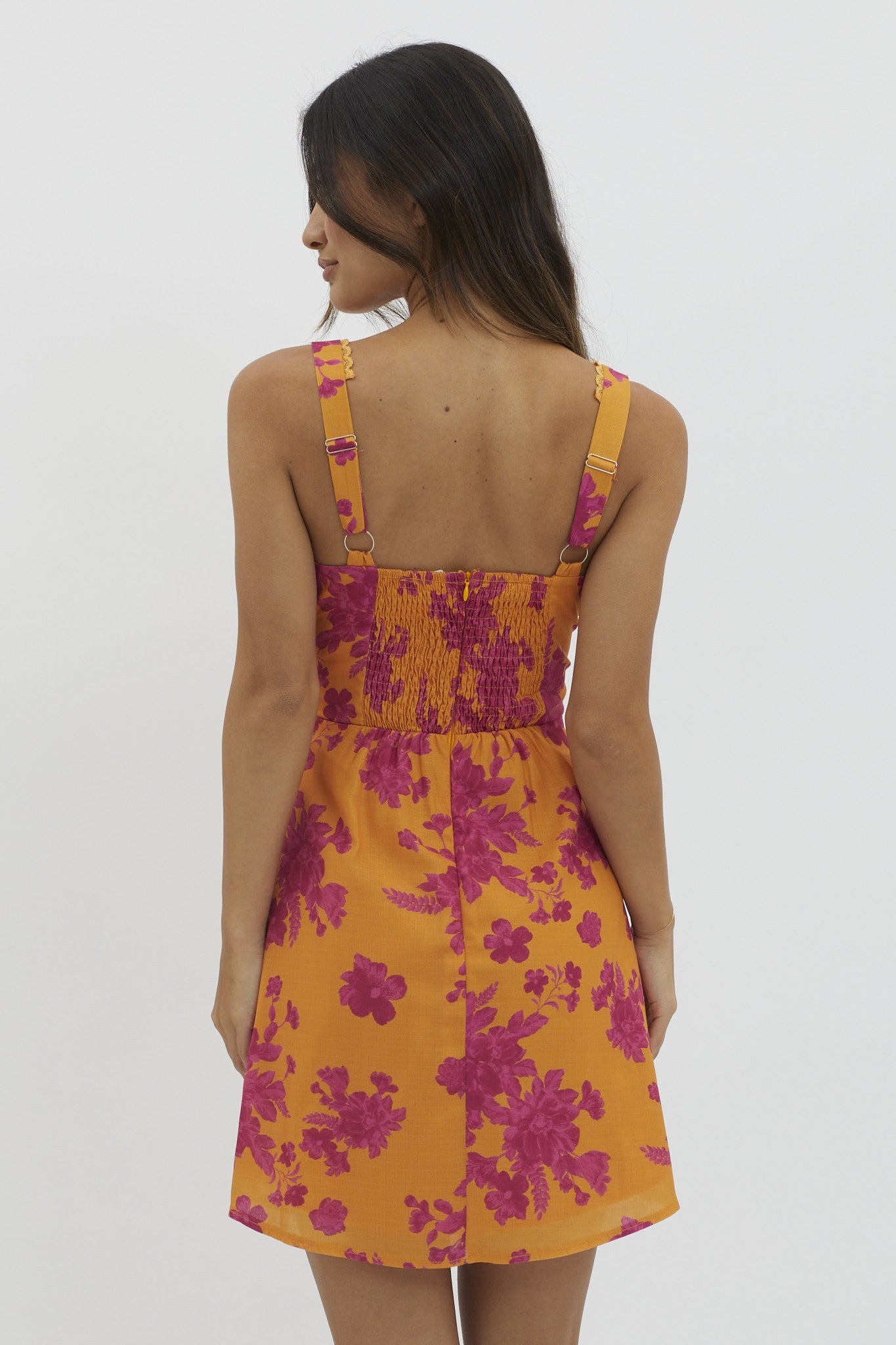 woman wearing a vibrant yellow floral sundress with pink patterns and a smocked back detail