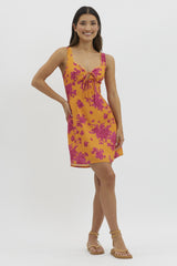 woman wearing a bright orange floral dress with pink accents and a tie front detail