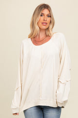 woman wearing a cream oversized long sleeve top with ribbed detailing and tie accents, paired with blue jeans
