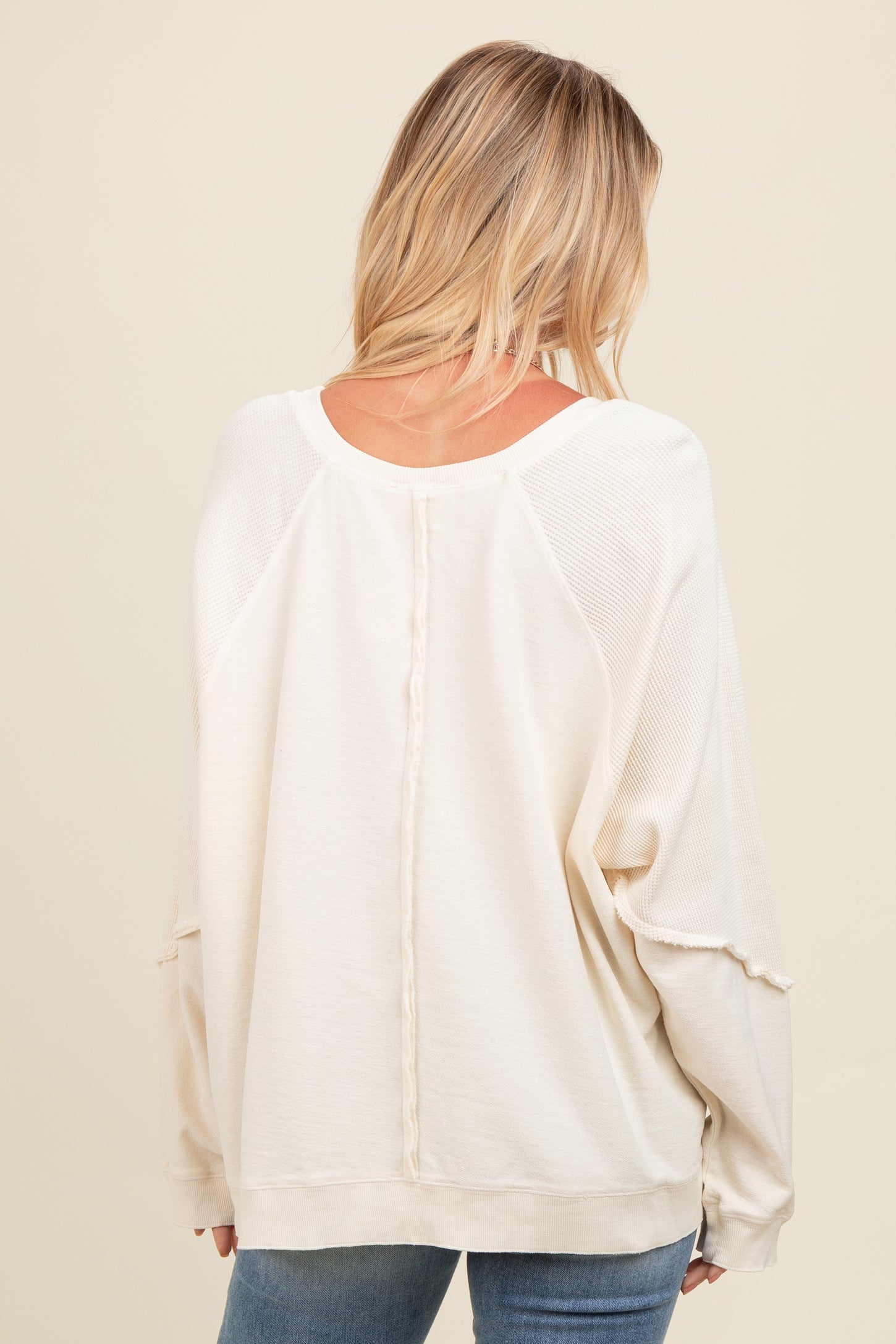 woman wearing a cream oversized sweater with a textured back and relaxed fit, styled with blue jeans
