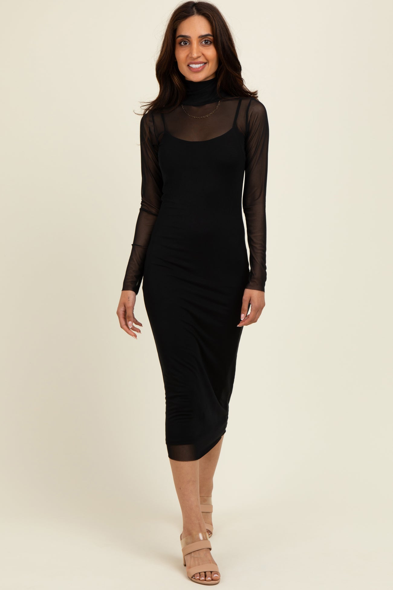 woman wearing a black fitted midi dress with sheer long sleeves and a mock neck, paired with nude heeled sandals
