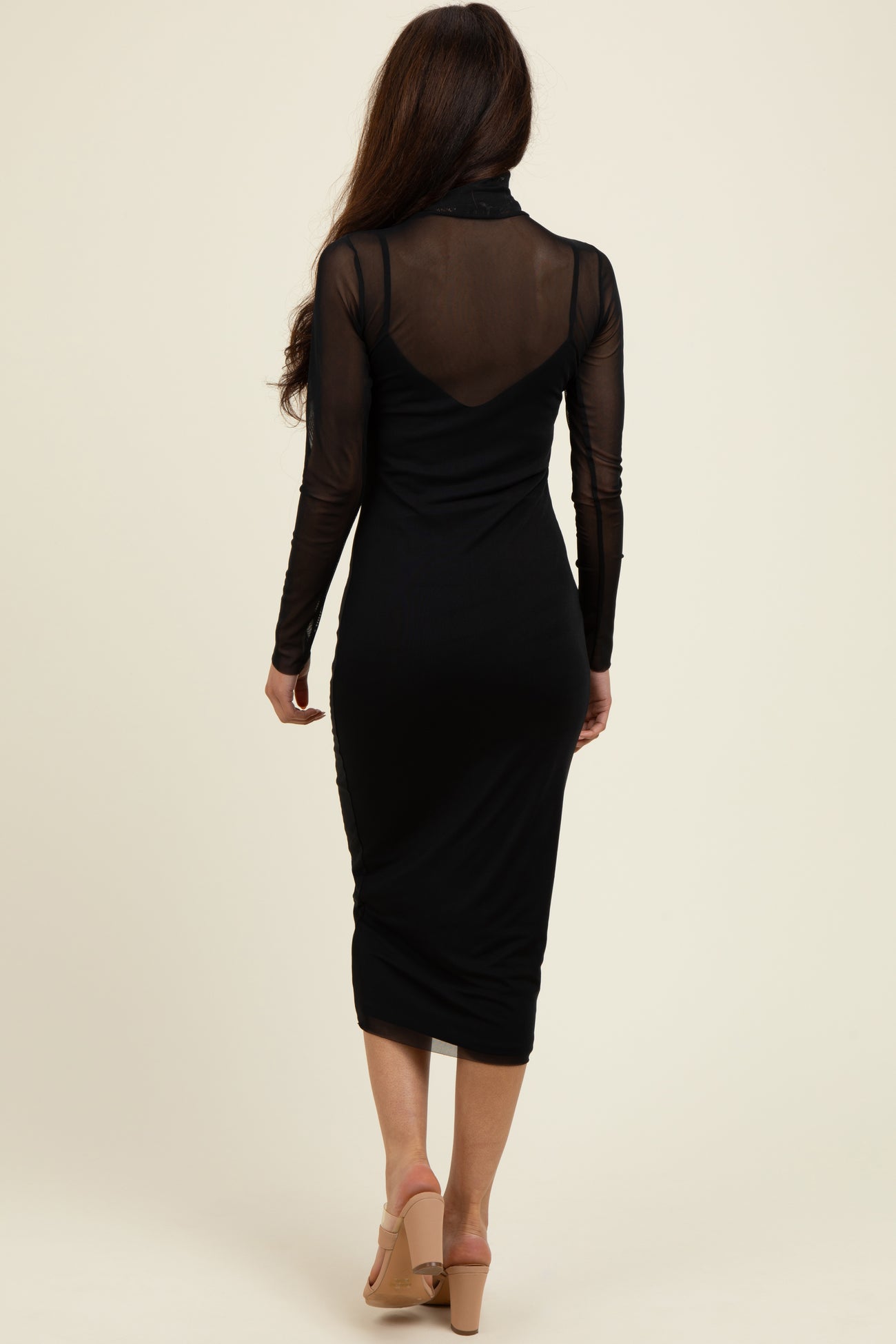 woman wearing a fitted black midi dress with long sheer sleeves and a high neckline, shown from the back