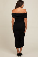 woman wearing a sleek black off-the-shoulder maternity dress with ruched detailing, showing a baby bump from the back