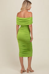woman wearing a fitted off-the-shoulder lime green ruched dress, styled with strappy sandals, viewed from the back