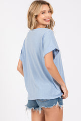 woman wearing a light blue oversized t-shirt and denim shorts, smiling and facing slightly away from the camera