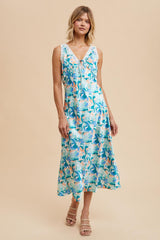 woman wearing a blue floral sleeveless maxi dress with lace detailing and a tie front, styled with neutral sandals