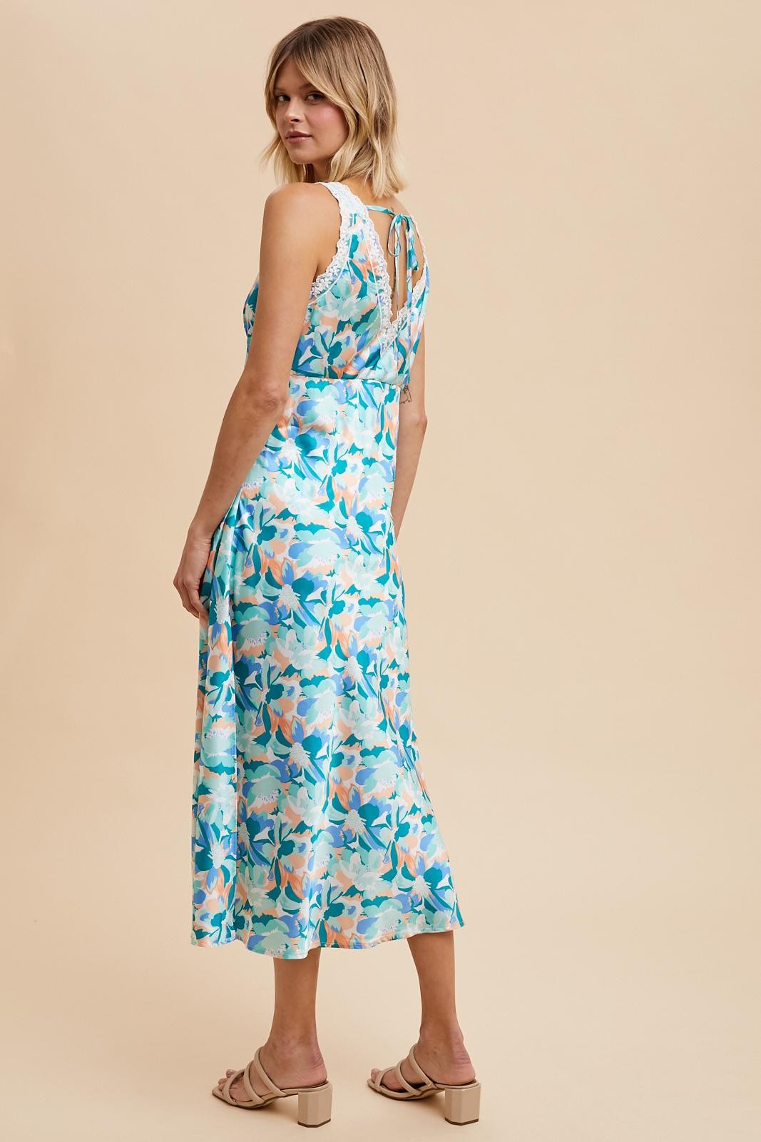 woman wearing a blue floral midi dress with a keyhole back and relaxed fit, standing against a beige background