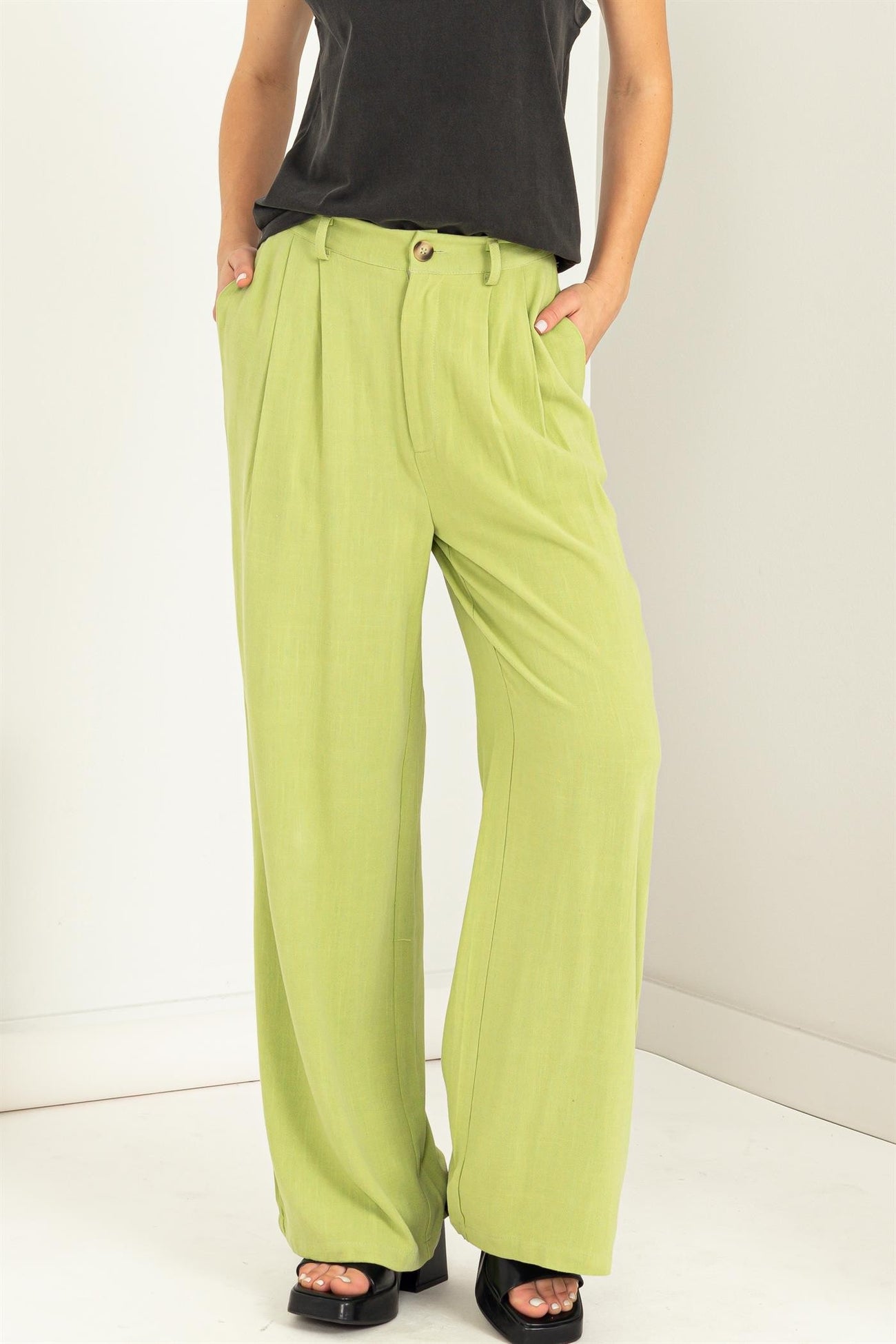 woman wearing green wide-leg trousers with pleats and a button detail, paired with a black top