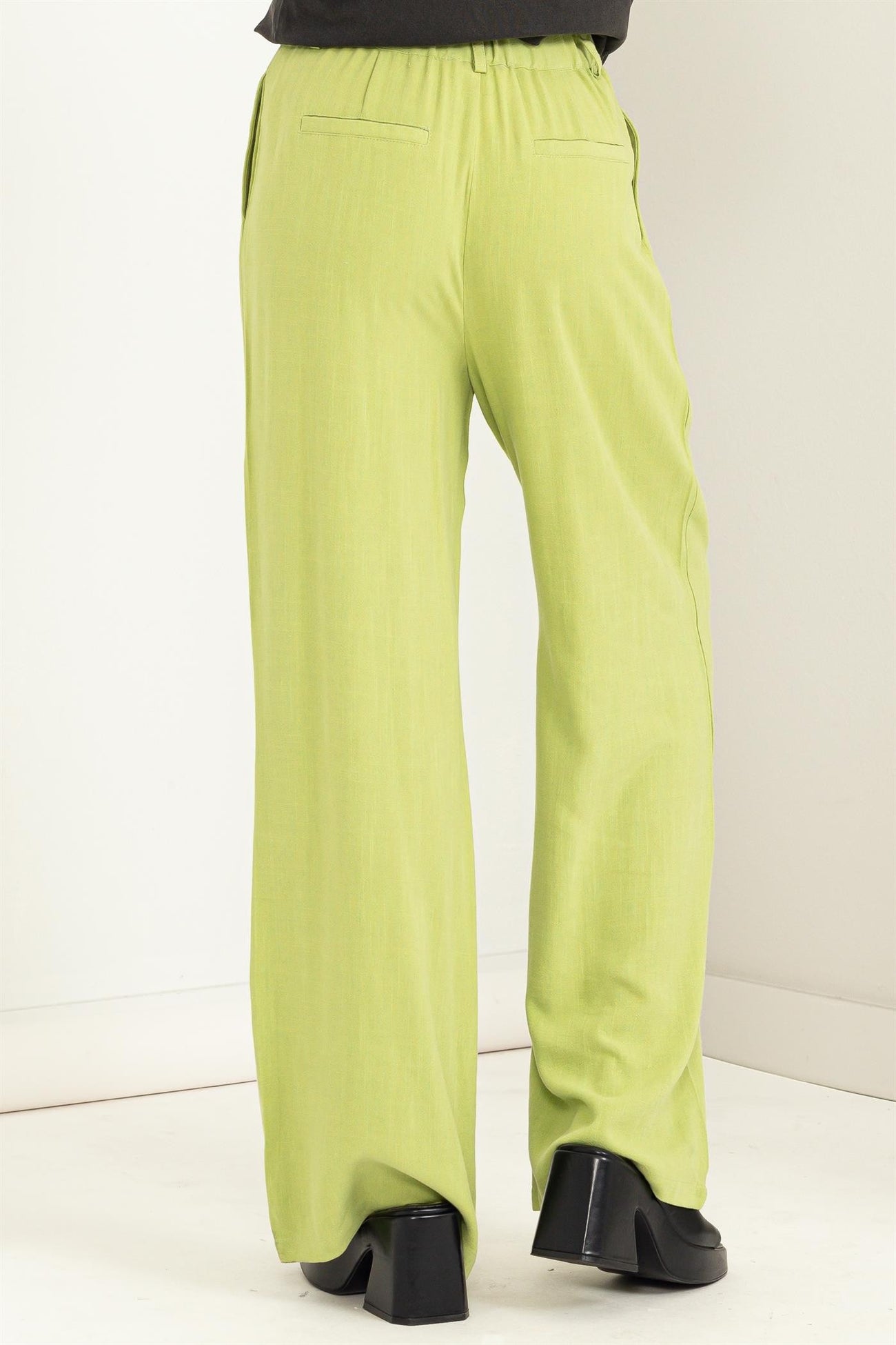 woman wearing high-waisted light green wide-leg pants, showing back view and stylish black heels