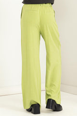 woman wearing high-waisted light green wide-leg pants, showing back view and stylish black heels