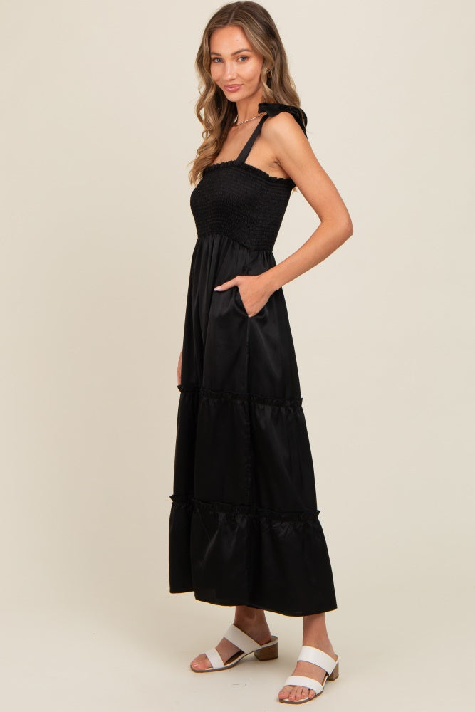 woman wearing a black tiered maxi dress with a smocked bodice and shoulder ties, showing side pockets