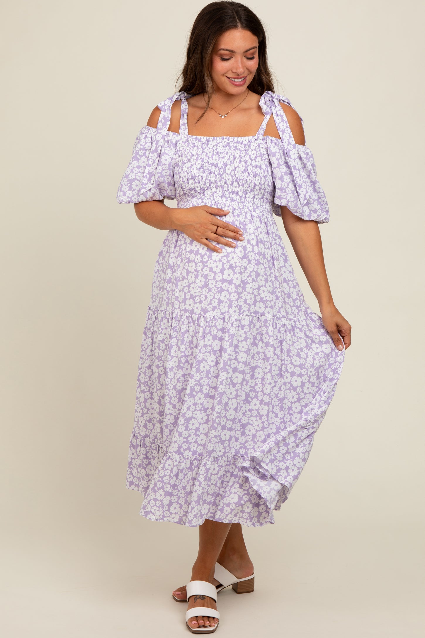 woman wearing a purple floral maternity dress with off-the-shoulder sleeves and holding her baby bump