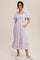 woman wearing a lavender floral print midi dress with puff sleeves and a smocked bodice, standing with one hand in a pocket