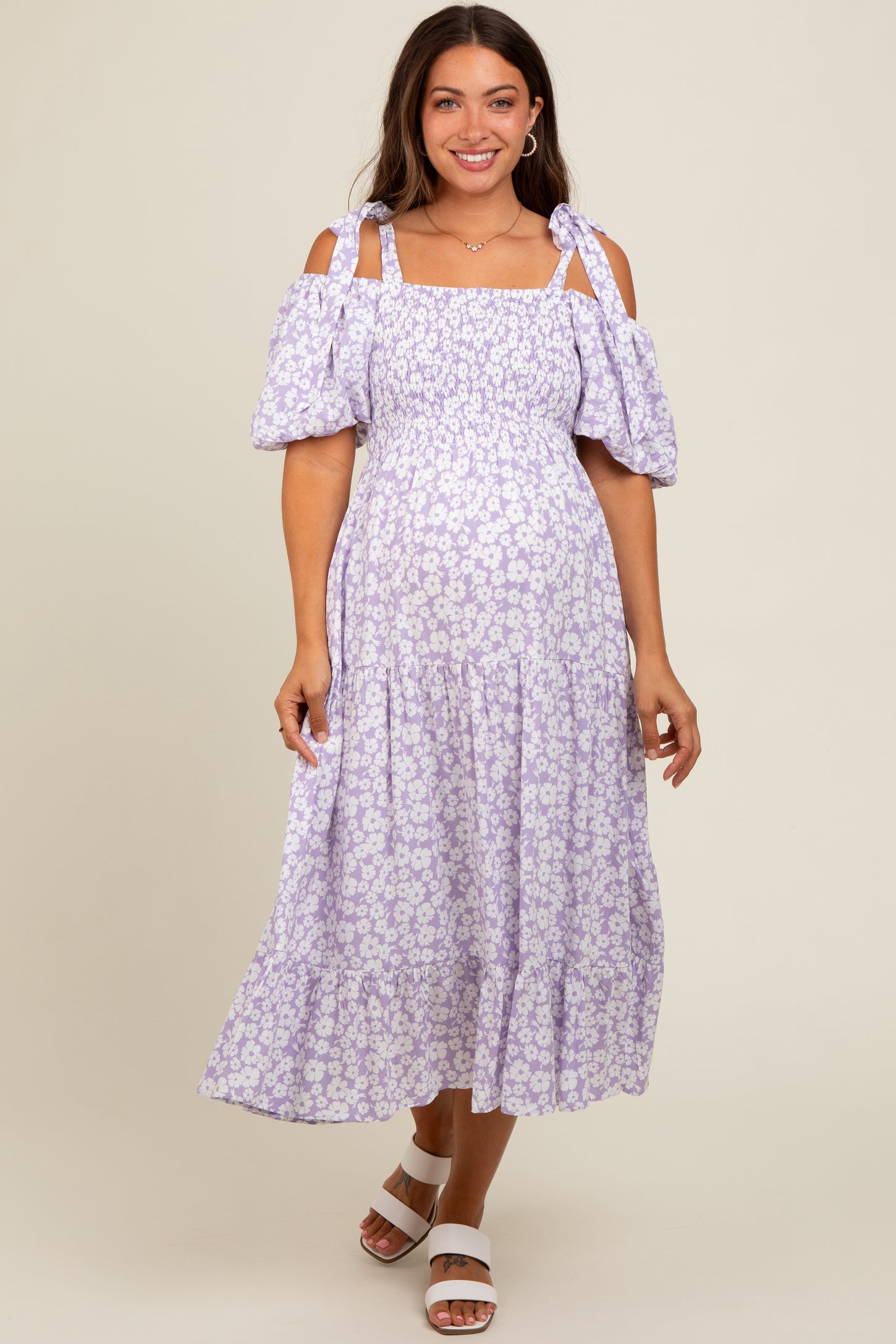woman wearing a lilac floral cold shoulder maternity dress with puff sleeves and a tiered skirt