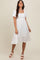 woman wearing a white puff sleeve midi dress with floral embroidery and a tiered hem, smiling and standing against a neutral background