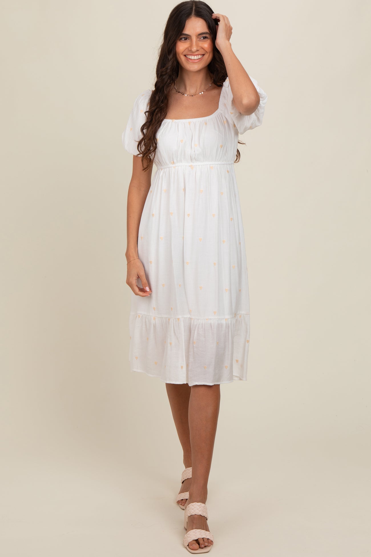 woman wearing a white midi dress with puff sleeves and embroidered details, standing against a neutral backdrop
