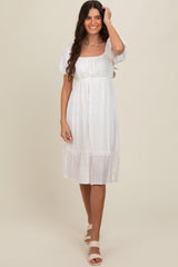 woman wearing a white midi dress with puff sleeves and embroidered details, standing against a neutral backdrop