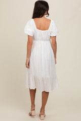 woman wearing a white midi dress with puff sleeves and a ruffled hem, shown from the back