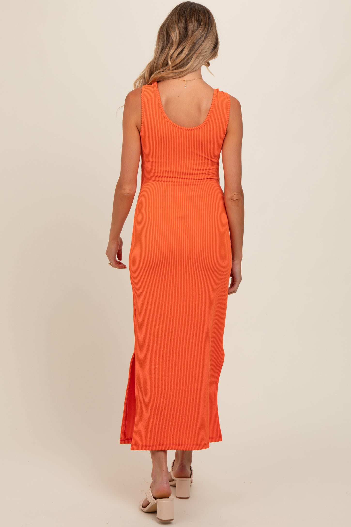 woman wearing a ribbed orange maternity maxi dress with a slit and a fitted silhouette, showing a baby bump