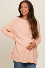 woman wearing a light peach maternity top and holding her baby bump