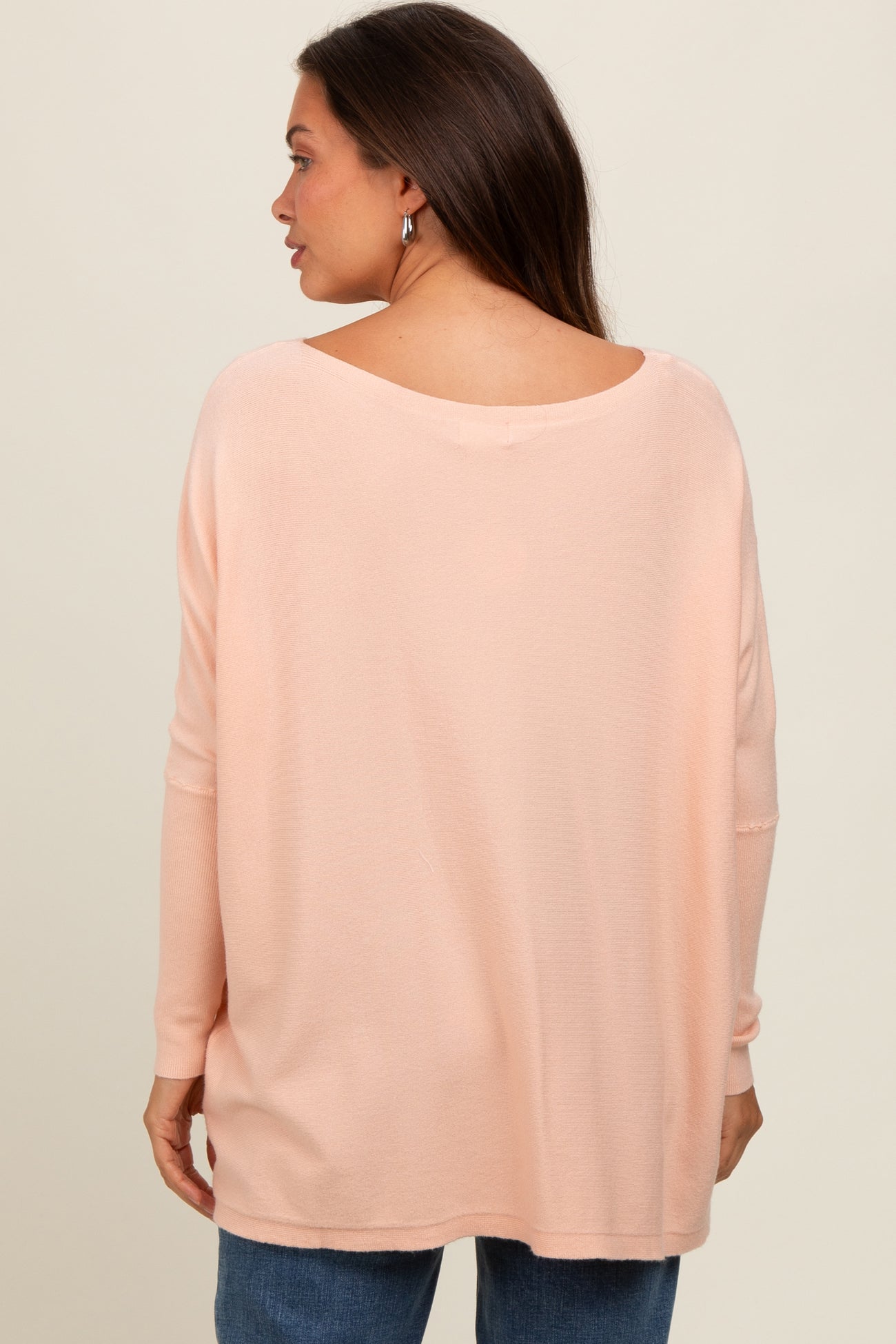 woman wearing a loose-fitting light pink maternity top with a wide neck and long sleeves