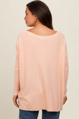 woman wearing a loose-fitting light pink maternity top with a wide neck and long sleeves