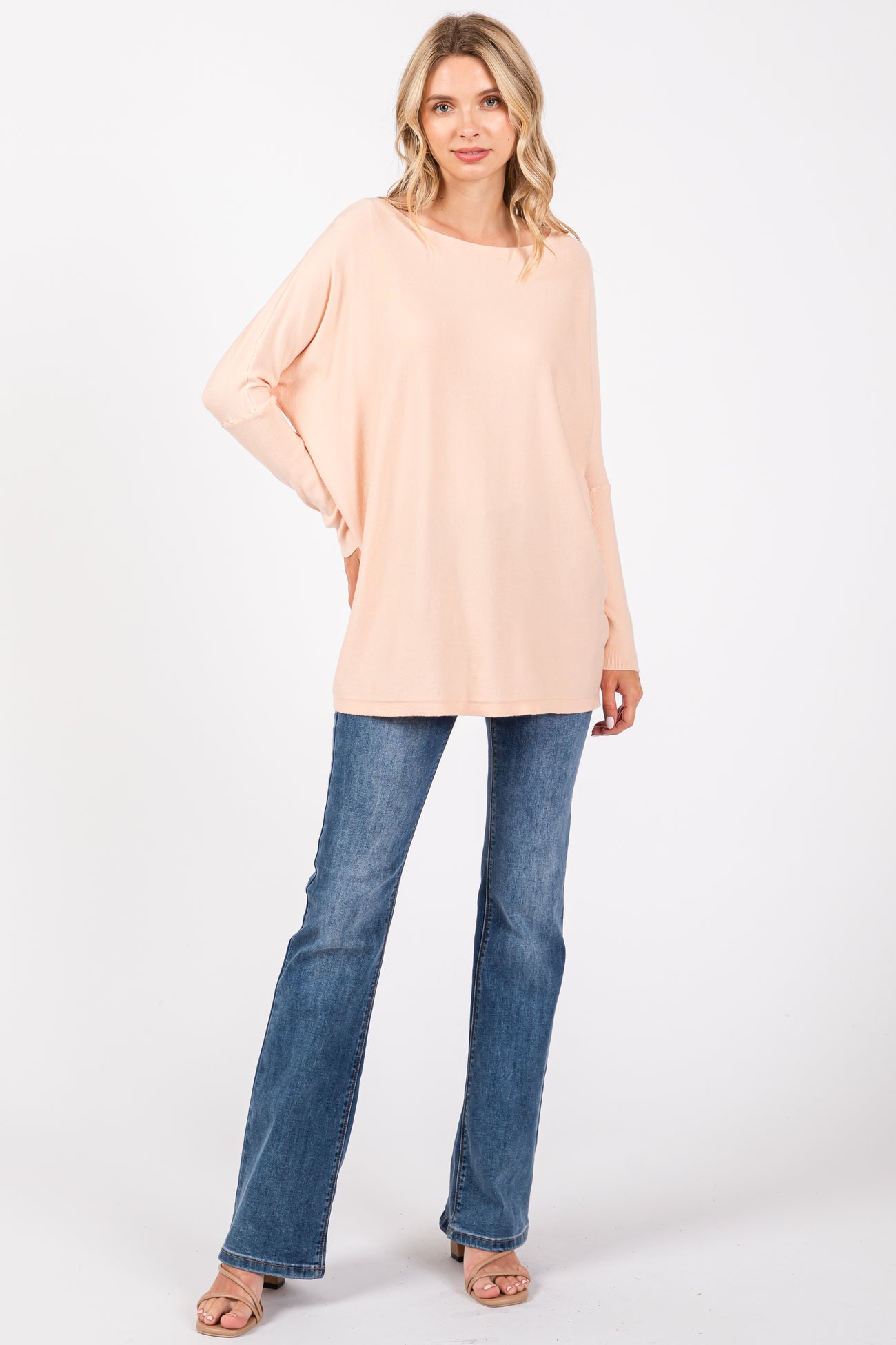woman wearing a light peach oversized long sleeve top and blue flared jeans