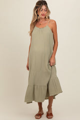 woman wearing a sage green maternity dress with adjustable straps and a tiered skirt, showing her baby bump