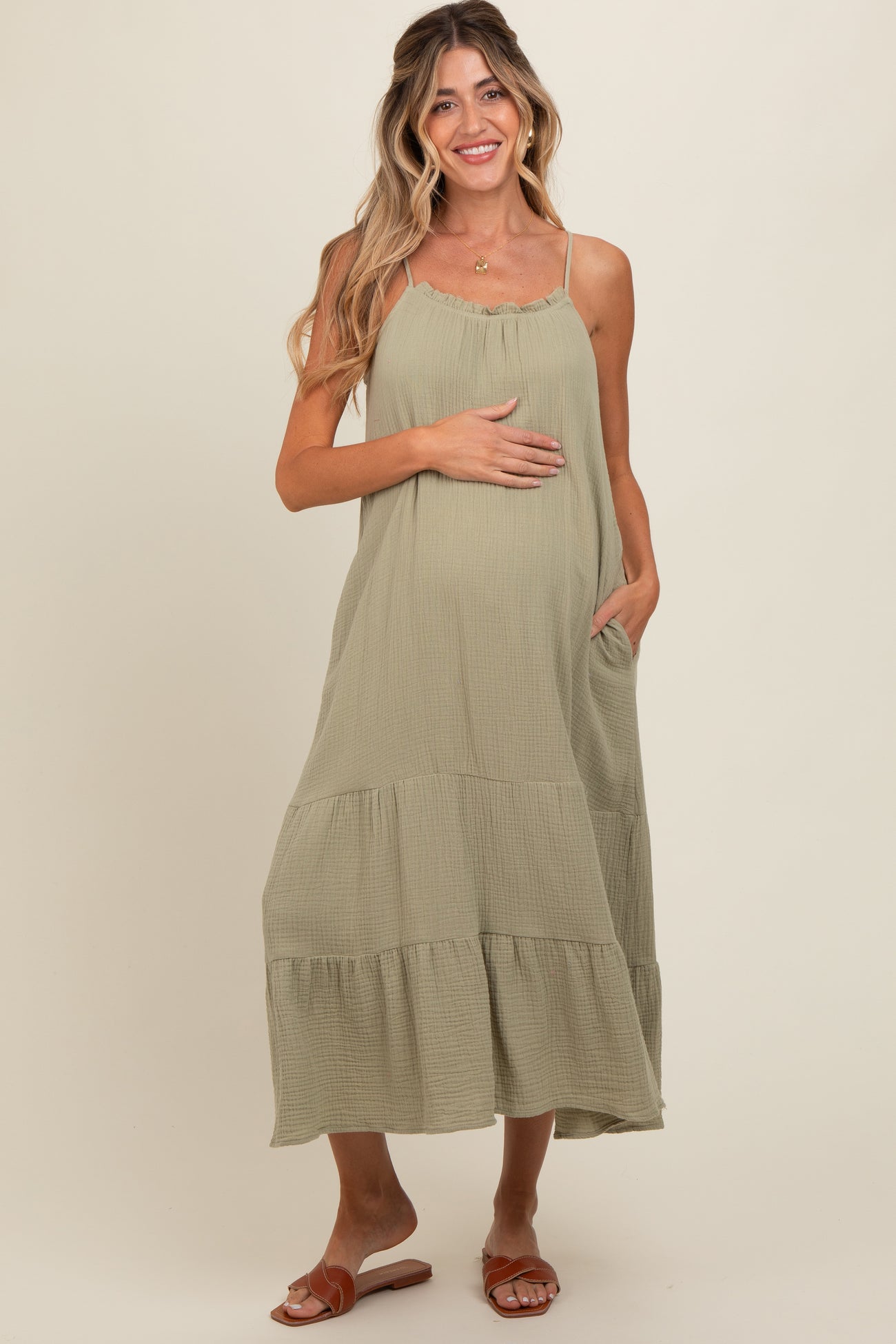 woman wearing a light olive green maternity maxi dress with a scoop neck and tiered style, showing her baby bump