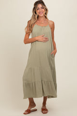 woman wearing a light olive green maternity maxi dress with a scoop neck and tiered style, showing her baby bump