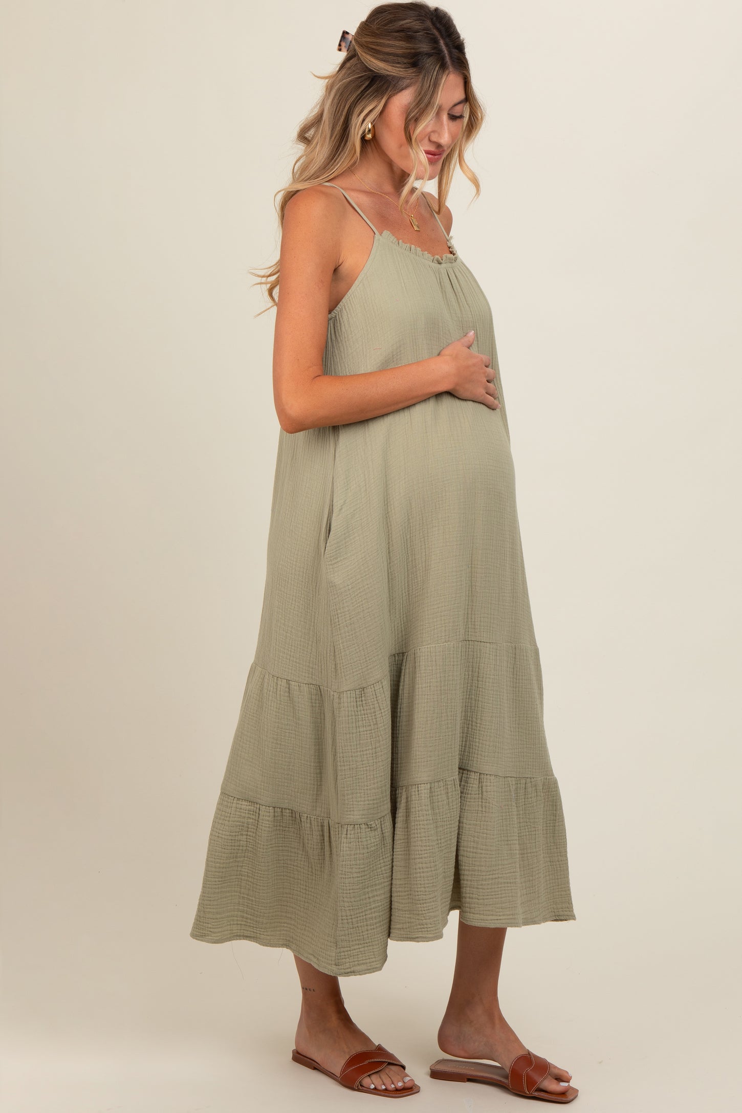 woman wearing a sage green tiered maternity dress and holding her baby bump