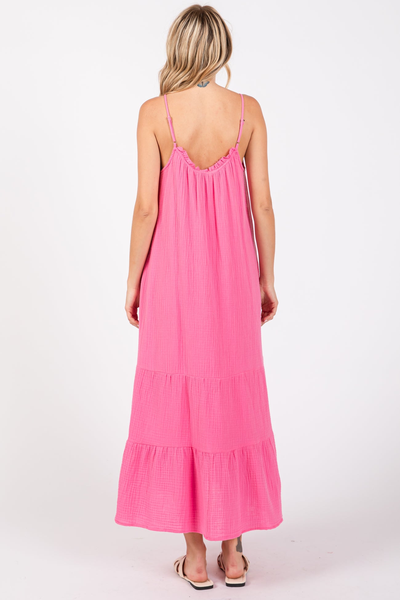 woman wearing a bright pink maxi dress with spaghetti straps and tiered ruffle details, viewed from the back