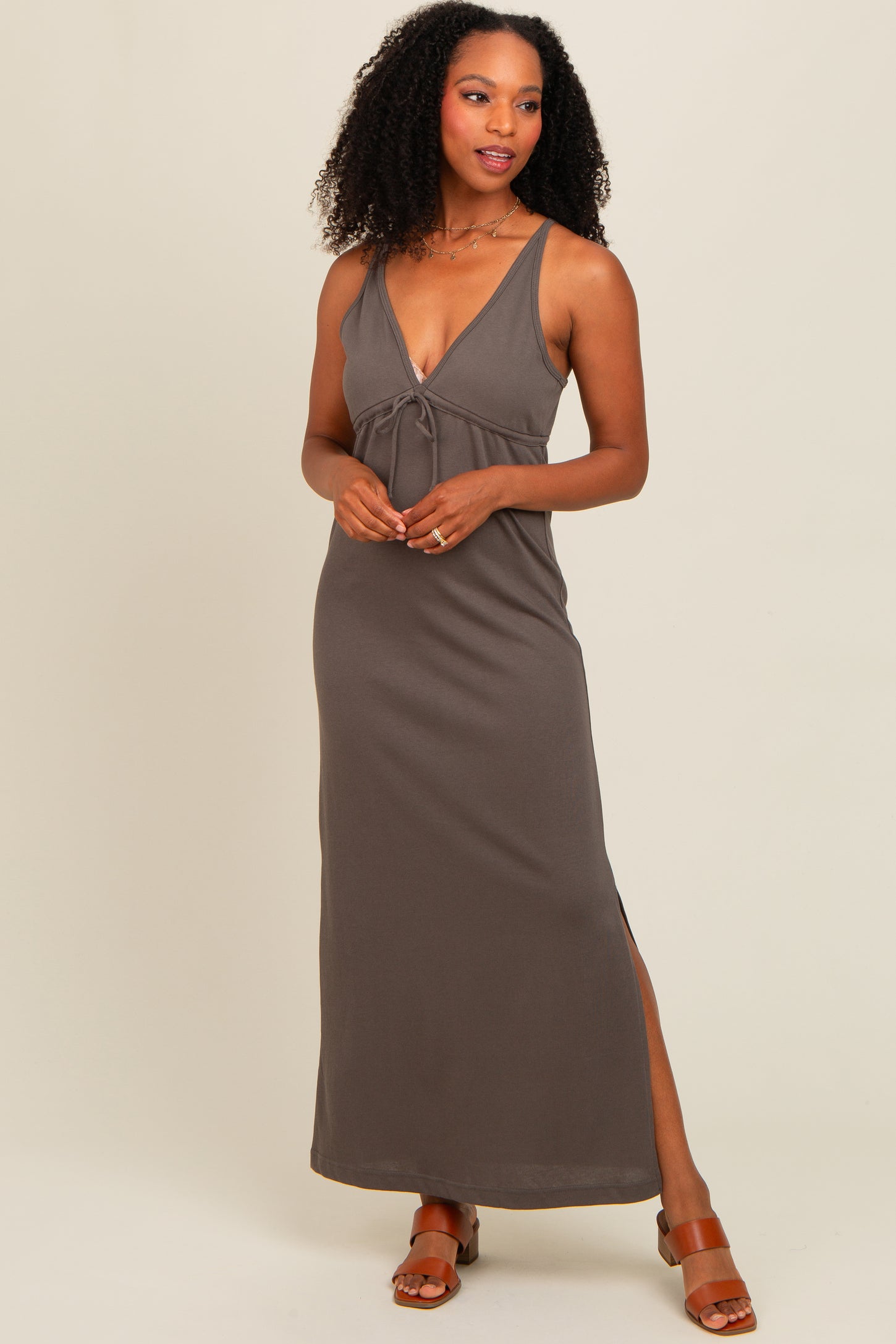 woman wearing a dark brown sleeveless maxi dress with a deep v-neck and side slit, standing with one hand on her hip