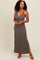 woman wearing a dark brown sleeveless maxi dress with a deep v-neck and side slit, standing with one hand on her hip