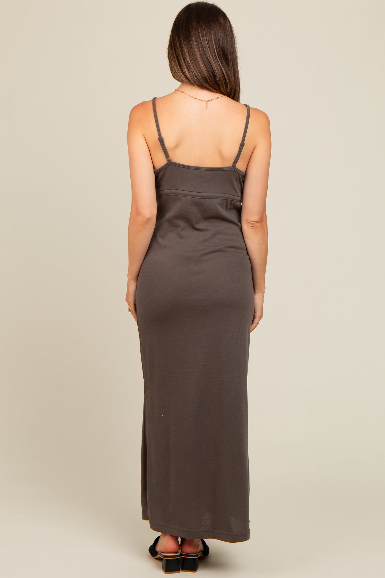 woman wearing a brown spaghetti strap maternity maxi dress, showing a fitted silhouette from the back