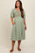 woman wearing a sage green maternity dress with puff sleeves and smocked bodice, posing with one hand in pocket