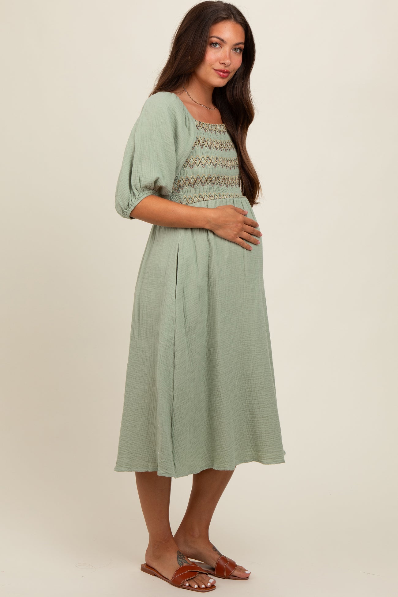 woman wearing a sage green short sleeve maternity dress with smocking detail and holding her baby bump