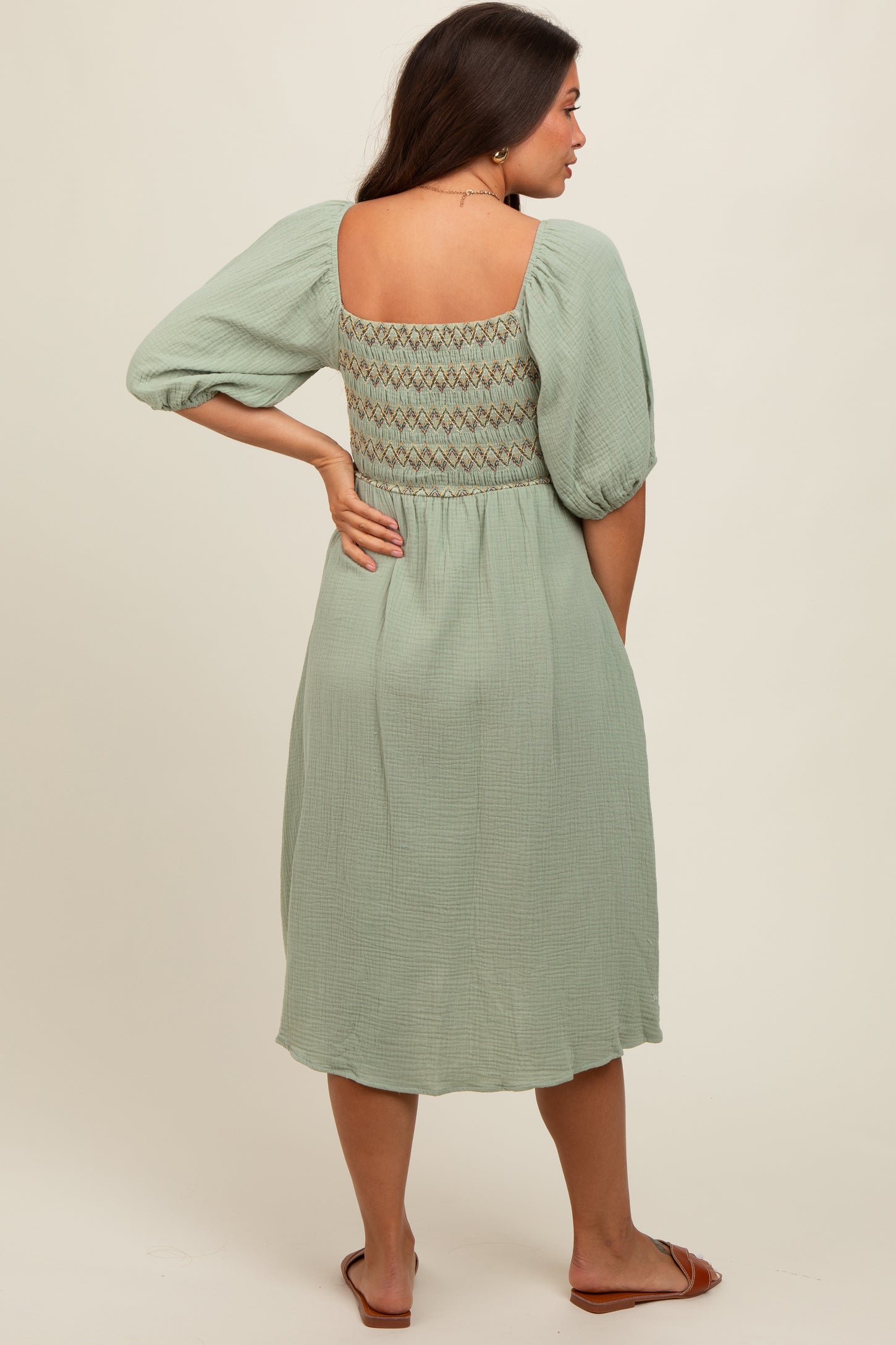 woman wearing a sage green maternity dress with puff sleeves and a lace-back detail, showing a baby bump