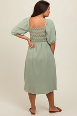 woman wearing a sage green maternity dress with puff sleeves and a lace-back detail, showing a baby bump