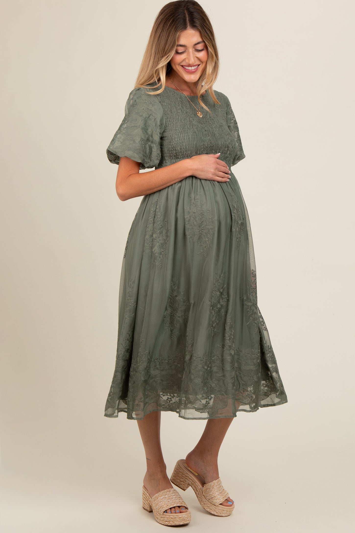 woman wearing an olive green lace maternity dress and holding her baby bump