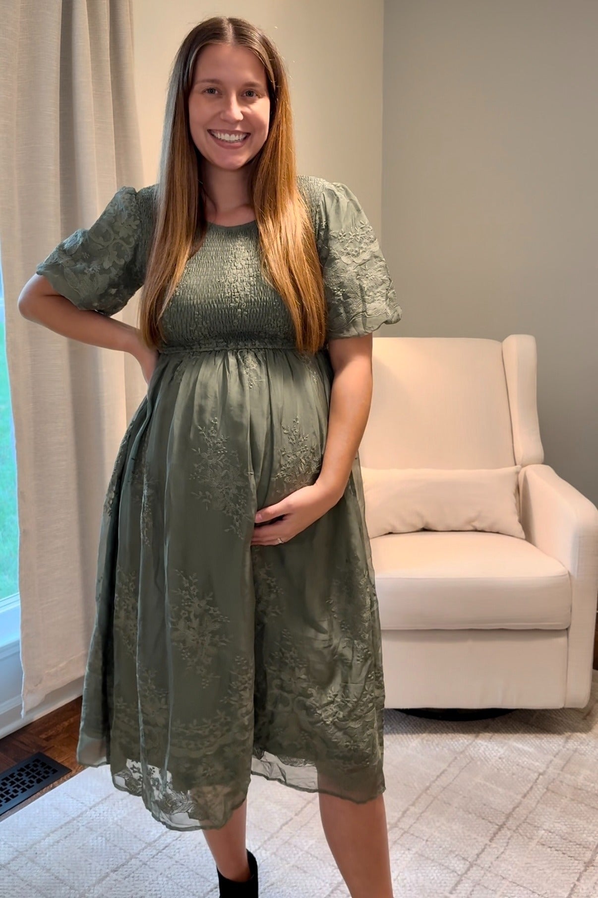 woman wearing a green embroidered maternity dress, showing baby bump, standing with hand on her hip