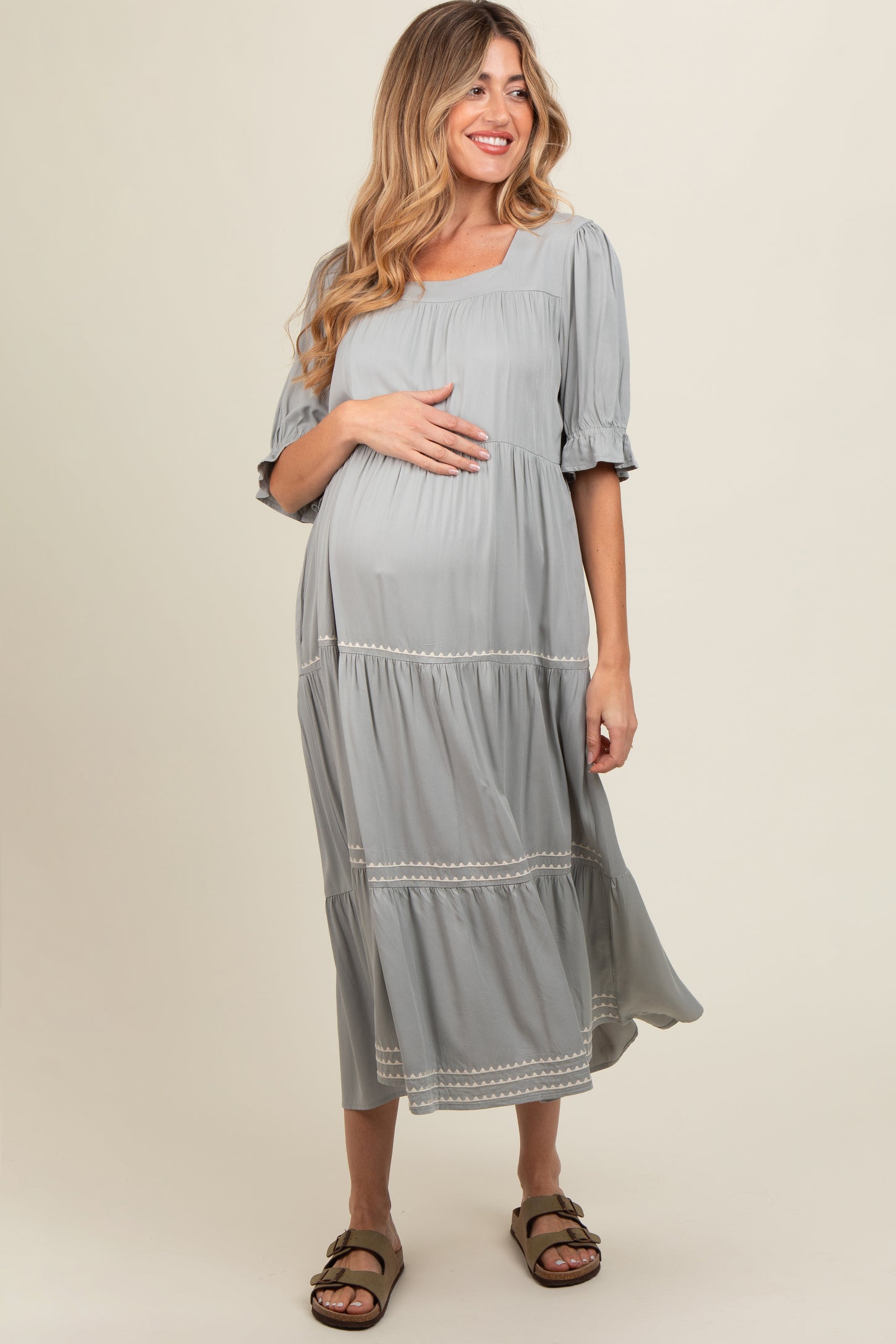 woman wearing a grey maternity dress with short puff sleeves and tiered skirt, gently holding her baby bump